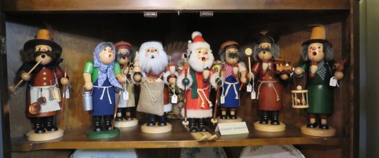 Lineup of wooden figurines with weird round holes for mouths. Two Santas stand in the middle.