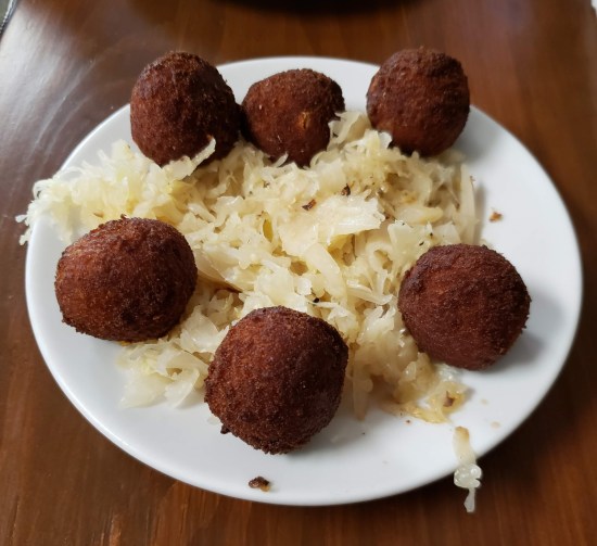 Six sauerkraut balls fried golden brown and served on a small plate with sauerkraut.