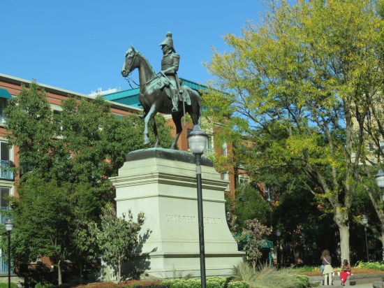 A statue of William Henry Harrison on horseback, on a tall concrete pedestal in the middle of a park.