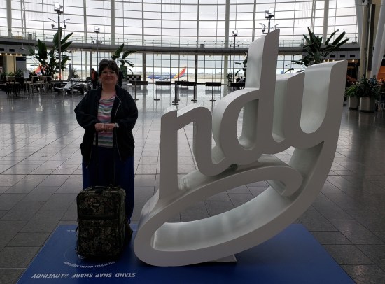 Anne wearing business clothing and standing in the concourse of Indianapolis International Airport next to the large letters N, D, and Y.