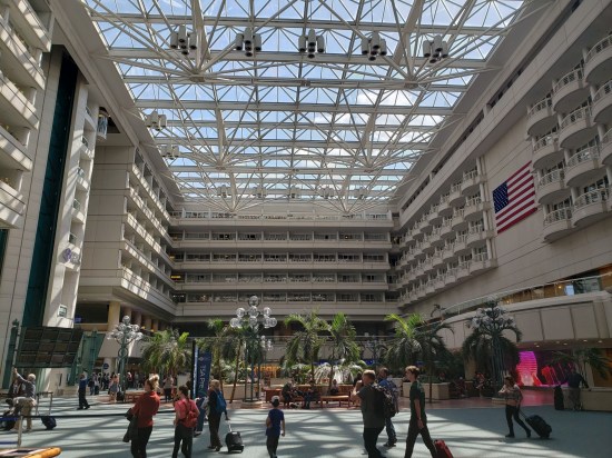 Airport interior with a five-story courtyard and palm trees indoors. Lots of people milling.