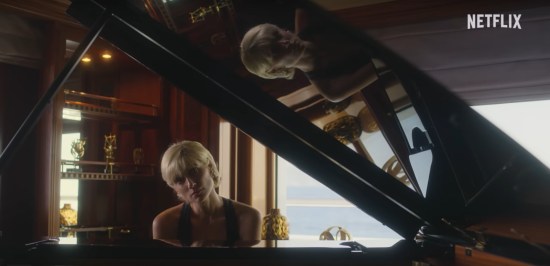 Princess Diana seated at a black piano with a hesitant expression. The open lid is shiny enough to contain her reflection, tilted 90 degrees widdershins. At upper right is the Netflix logo.