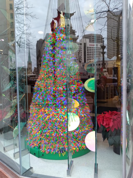 Four-foot Christmas tree that's all lights and no wood or needles, in a store window. Reflections of tall ball buildings behind us oscure some of the window display.
