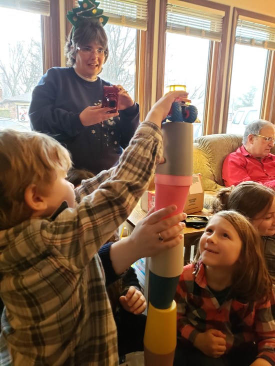 My wife Anne decked out in Christmas regalia, trying to photograph tiny kids stacking plastic cups into a tower.