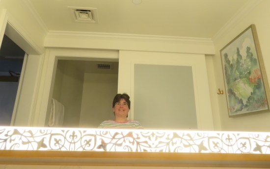 Selfie of Anne in our Disney Resort bathroom mirror. Fancy trim glows around the perimeter. A Mary Poppins-themed painting hangs at right.