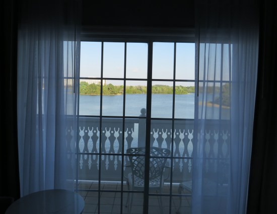 Through diaphanous white curtains is the balcony, which has a white balustrade and a water view not fully visible through the curtains.
