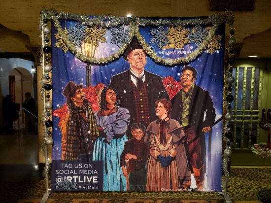 Painted backdrop of "A Christmas Carol" diverse cast recommending we tag our shares with @IRTLive or #IRTCarol.