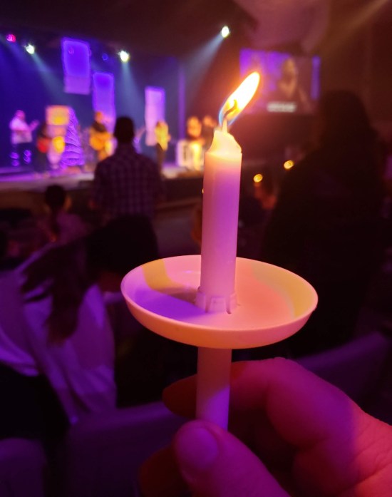me holding a lit candle in a darkened church auditorium.  A band is onstage in the distant background, in blue and purple lighting.