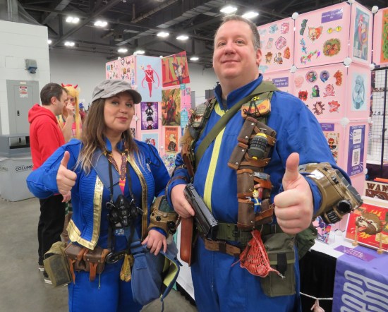 Husband and wife in blue jumpsuits and covered in imitation Fallout in-game items.