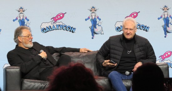 Frakes and Spiner sharing a couch. Frakes has a mic; Spiner has his phone out.