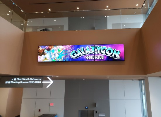Bright GalaxyCon sign mounted on the wall above the bottom end of the escalators.