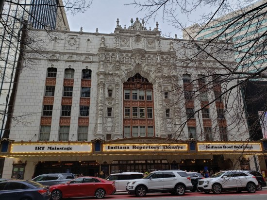 Grand old facade of the Indiana Repertory Theatre. Lots of ornately carved stonework. Traffic is busy out front.