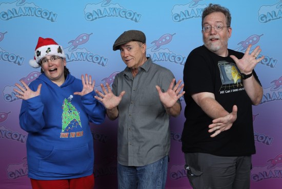Us doing jazz hands with Jeffrey Combs, who's wearing a gray flat cap that matches his buttoned shirt. His expression is cautiously bemused.