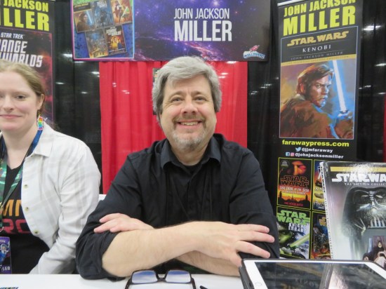 John Jackson Miller at his booth, smiling and with a big standee for his Obi-Wan Kenobi novel.