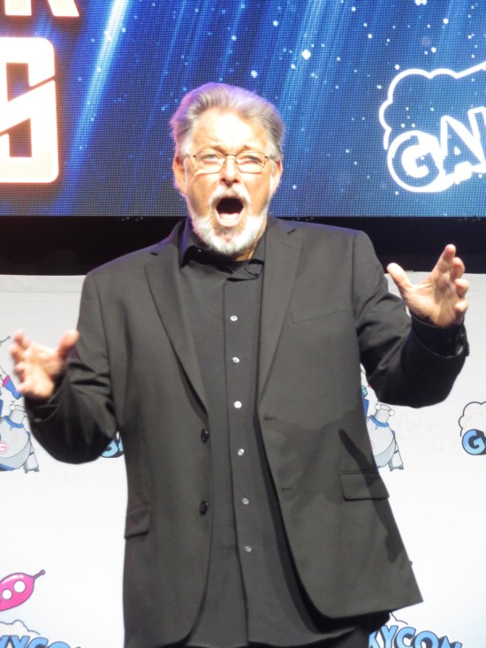 Jonathan Frakes on stage bombastically singing in an all-black suit, no tie.