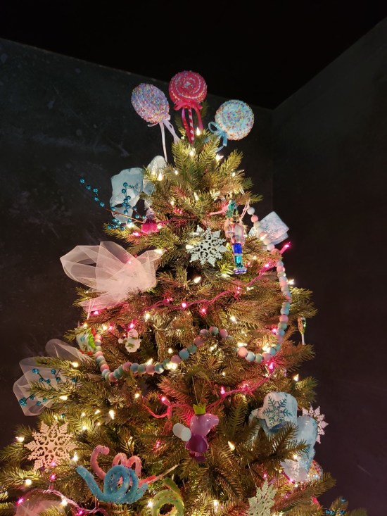 Top half of a Christmas tree with three big lollipops as toppers. The room is otherwise dark.