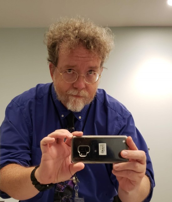 A selfie taken in a bathroom. I'm rolling my eyes, holding my phone with both hands, and wearing a purple dress shirt and Grateful Dead tie even though I don't like the Grateful Dead. It was a gift.