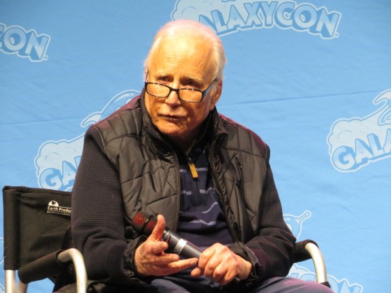 Richard Dreyfuss still sitting on stage, holding a mic and pondering his next answer.