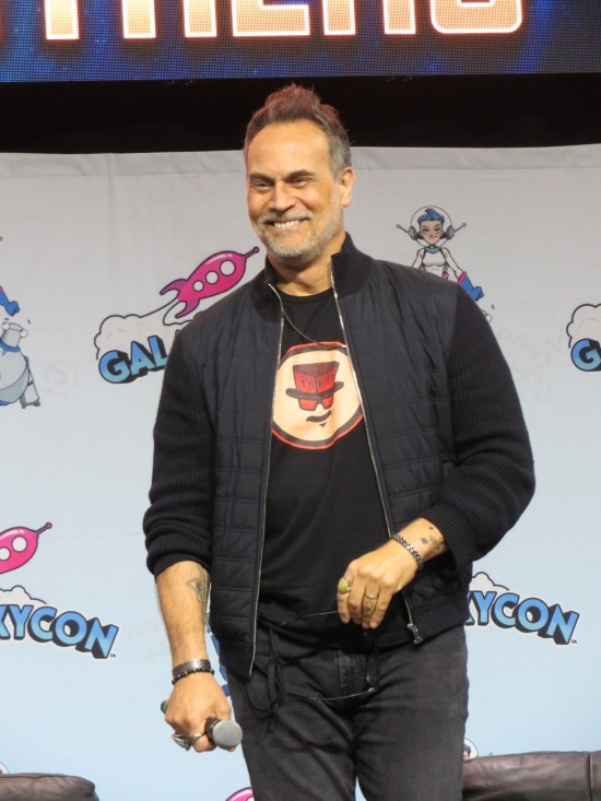 Todd Stashwick on stage, smiling and wearing a black jacket and T-shirt.