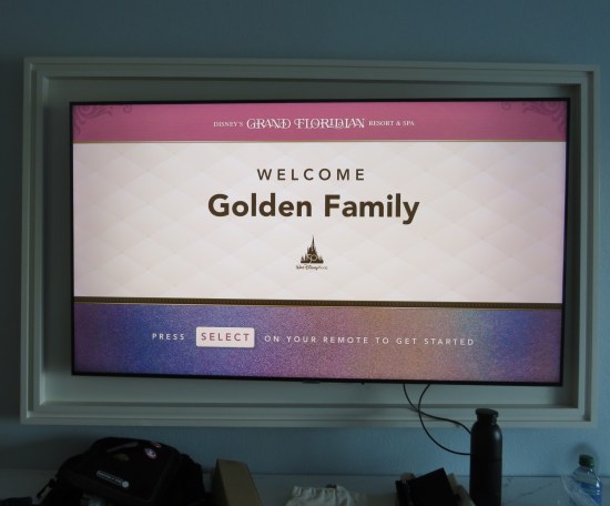 Hotel TV displaying message "Welcome Golden Family". At the top is the Disney's Grand Floridian Resort and Spa logo. In the middle is a Disney World 50th anniversary icon. At bottom the message "Press Select on your remote to get started."