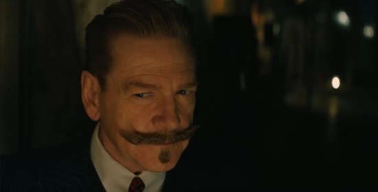 Kenneth Branagh wearing Hercule Poirot's distinctive facial hair side-eyes someone skeptically in the darkness.