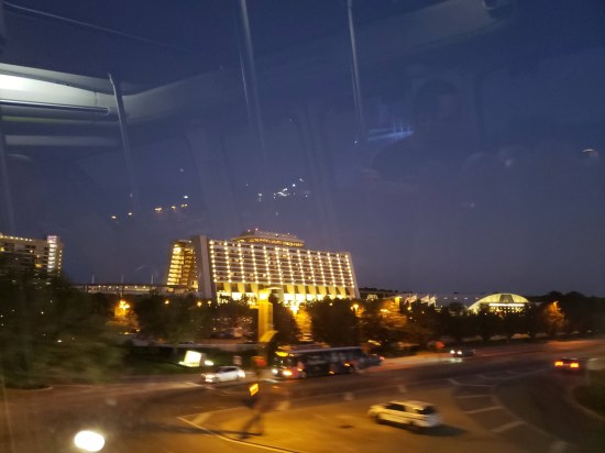 Nighttime hotel, gridllike walls all lit up. Sky is purple. Shot through a window with lots of interior reflections.