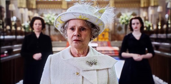 Imelda Staunton as Queen Elizabeth II dressed in white, standing in Westminster Abbey and contemplating the future. Hanging back on either side of her are Olivia Colman and Claire Foy, each in black as their respective Elizabeths from previous seasons.