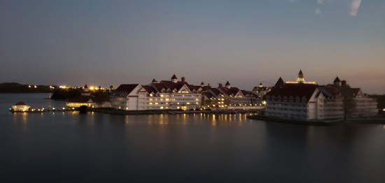 Wide evening shot of a large resort with many buildings along a lagoon. Lots of electric lights.