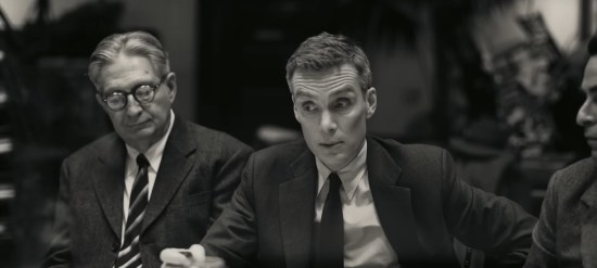 Cillian Murphy as J. Robert Oppenheimer in one of the black-and-white flashbacks. He's seated at a table, incredulous during testimony and reaching for his coffee mug.