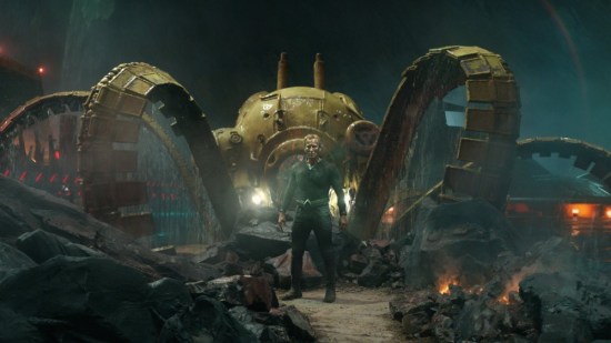 Patrick Wilson in his Ocean Master costume (no helmet) standing in front of a giant robot octopus rising from the depths.