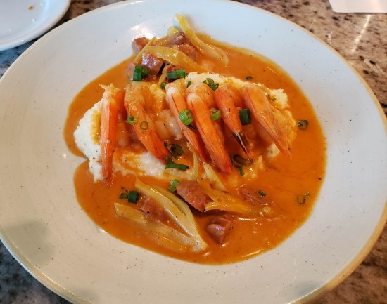 Bowl of orange grits with lots of shrimp on top.