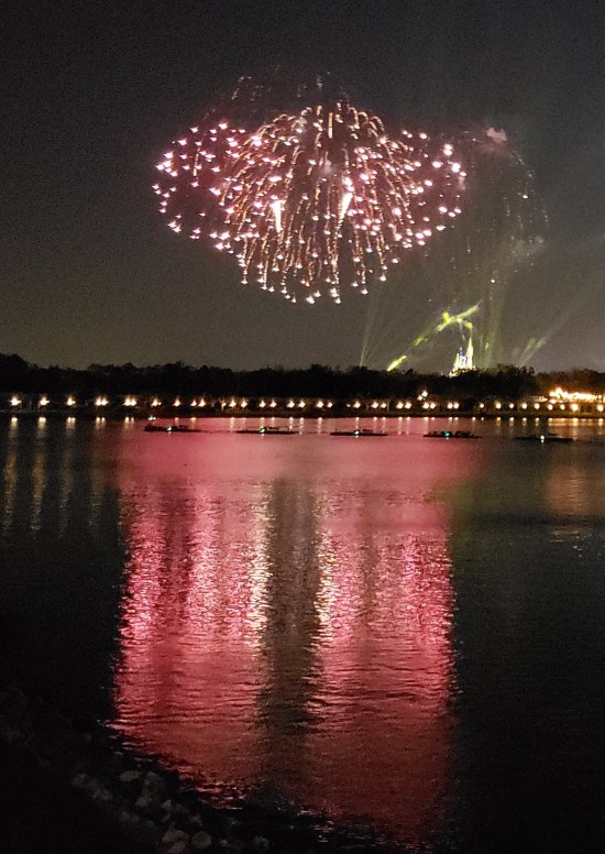 Distant fireworks over water. Red Mickey head, ears drooping. 
