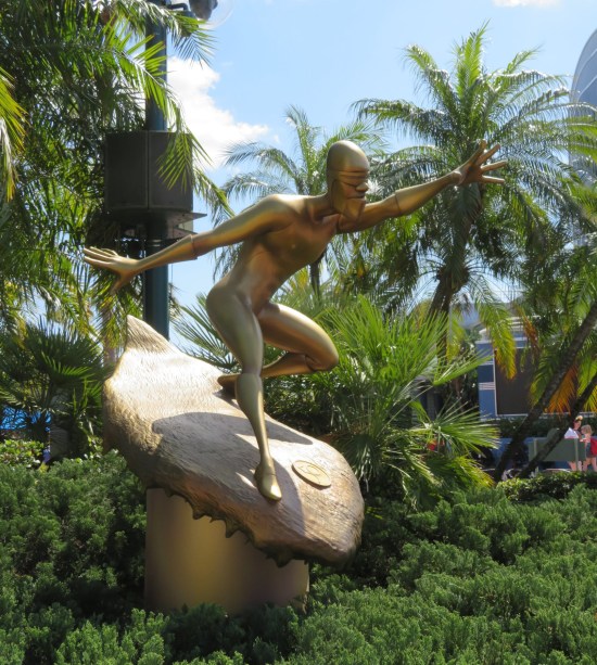 Gilded statue of a thin black superhero skating on an ice ramp. Lots of palm trees behind it.