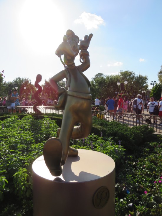 Gilded statue of Goofy, happily walking. The late afternoon sun is next to his head, so he's a bit shadowy.