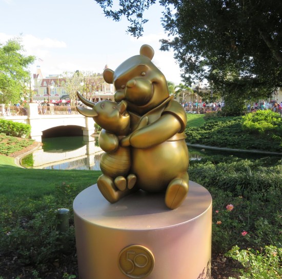 Gilded statue of Pooh and Piglet hugging. Behind them is a calm creek.