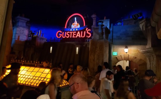 Long line indoors waiting for the Ratatouille ride. Decor includes an exterior facade of Gusteau's restaurant with neon signage.