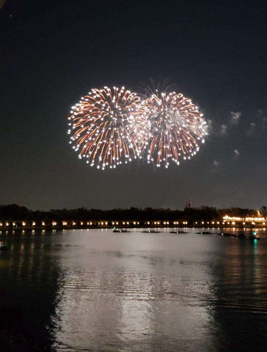Distant fireworks over water. Two white balls overlapping, one slightly larger.