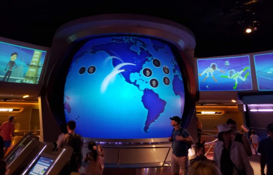 Science museum room with a large, squat, entirely blue Earth globe in the middle of the room. Small circles dot the electronic globe with photos of riders' faces, including my own.