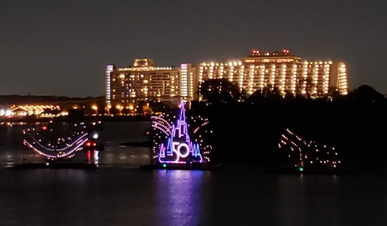 Boats carrying lights across nighttime water. All-purple version of DIsney World's official 50th anniversary logo.