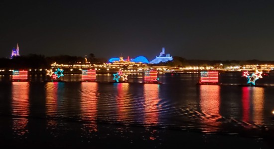 Boats carrying lights across nighttime water. Light-show shapes include stars and American flags.