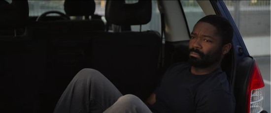 David Oyelowo sitting in an SUV trunk, looking forlorn.