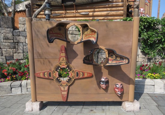 Totem pole pieces mounted on a board with head-shaped holes in the middle for amusement-park photo op use.