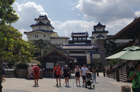 Long shot of much Japanese architecture in the theme park. Numerous guests walk here and there.