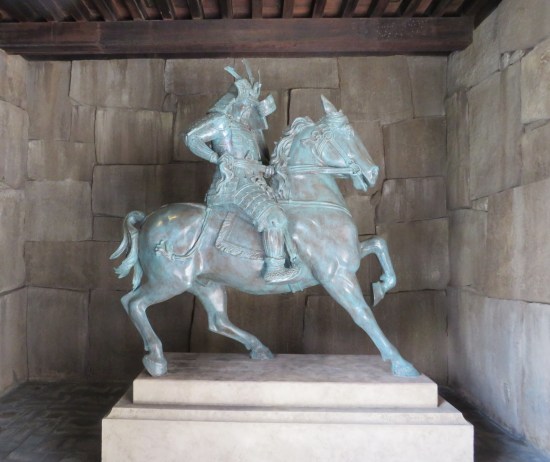 All-white, life-size Japanese horseman statue in a rock alcove.