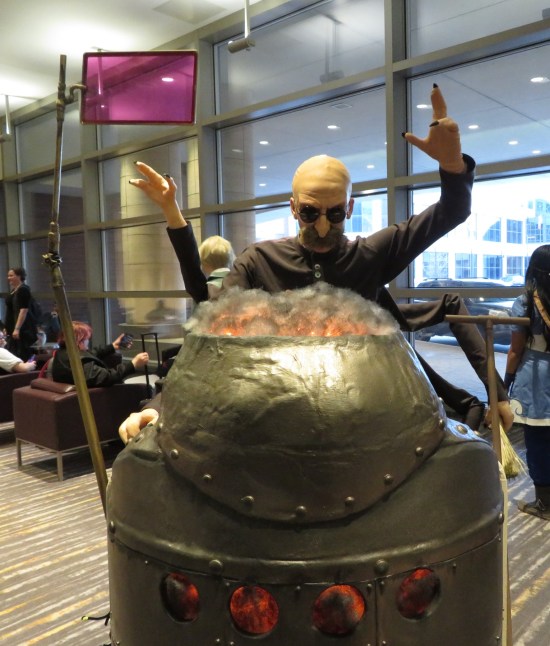 cosplay: bald mad scientist with mustache looming over a domed robot.