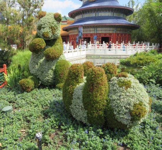 Topiary sculpture of two pandas, one sitting and one rolling on its back.