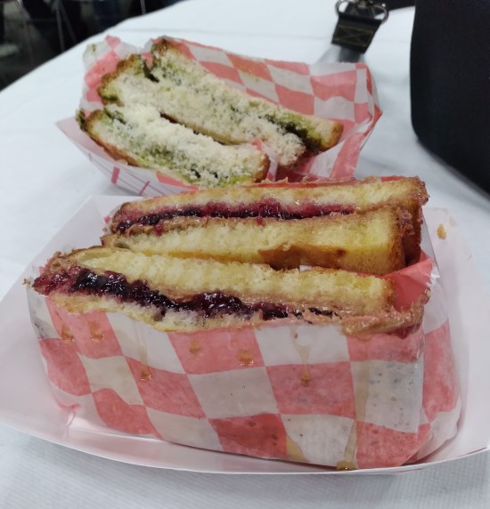 Two sandwiches on toast: one obviously PB&J, one with green contents between its bread slices.