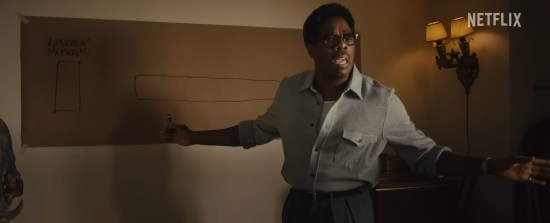 Colman Domingo playing Bayard Rustin, a Black man in a half-buttoned grey dress shirt, sleeves rolled up. He speaks before an offscreen crowd, gesturing a marker at a long piece of brown kraft paper taped on a wall. It will eventually be a primitive planning map of Washington DC; so far it only has a square for the Lincoln Memorial and a longer, unlabeled one for the reflecting pool.