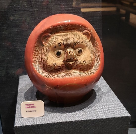 Statue of a happy bearlike animal's head inside a giant red grape or acorn or something.