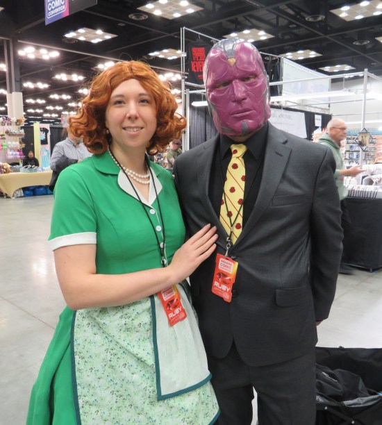 Cosplay: Scarlet Witch in green homemaker dress and white apron. The Vision with red android face and business suit with yellow tie.